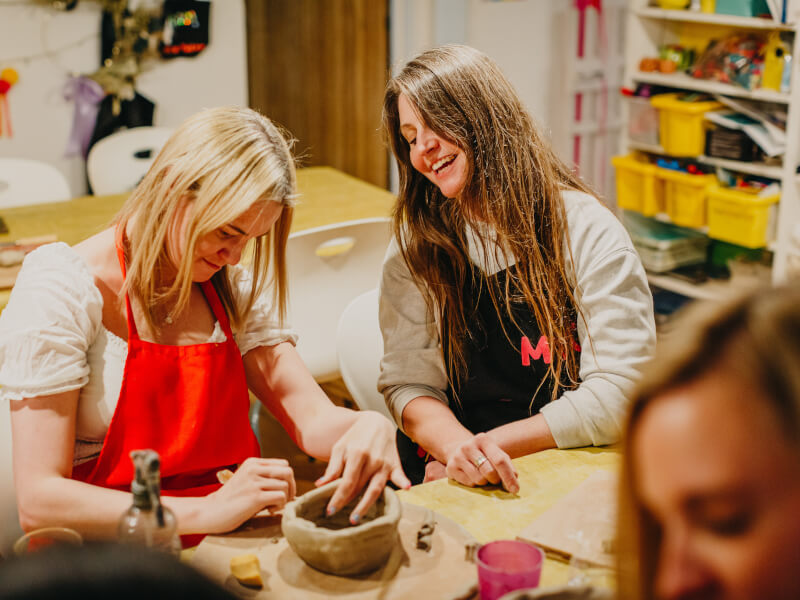 Two women in a pottery studio, one shaping a bowl